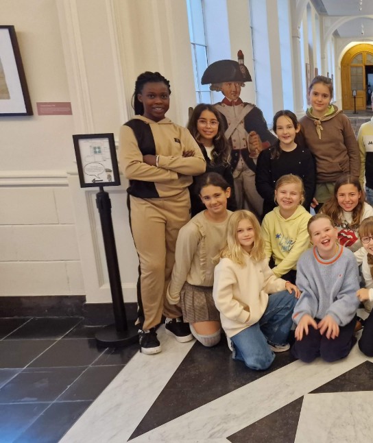 Groep lachende kinderen poseert in de abdij van Bornem met historische soldatenfiguren op de achtergrond. (vergroot foto)