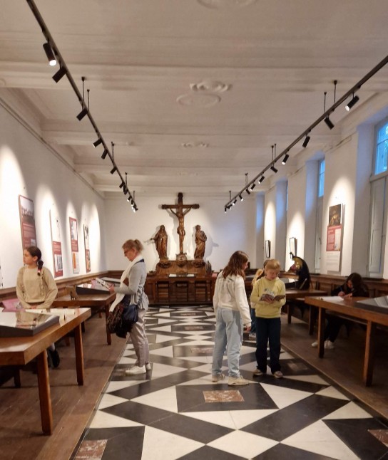 Mensen bekijken tentoonstellingen in de abdij van Bornem met een zwart-witte geometrische vloer en een kruisbeeld aan het einde. (vergroot foto)