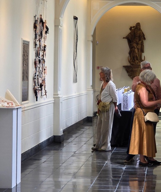 Drie bezoekers bekijken kunstwerken in de pandgang van de Abdij. (vergroot foto)