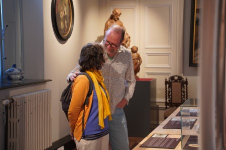 Twee mensen bekijken samen een tentoonstelling in de abdij van Bornem, met beeldhouwwerken en schilderijen op de achtergrond.