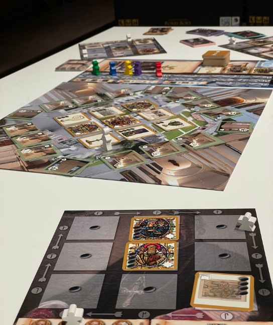 Bordspel met speelstukken en kaarten, verspreid over een witte tafel, met focus op een spelersbord op de voorgrond. (vergroot foto)